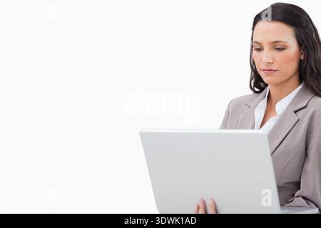 Woman in light gray blazer holding silver laptop, focusing on screen at white backdrop, copy space. Female, jacket, professional, minimalist, highkey, Stock Photo