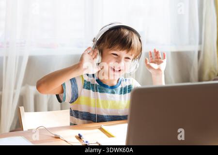 child boy in earphones is using a laptop and study online at home. homeschooling, distant learning || Model released Stock Photo
