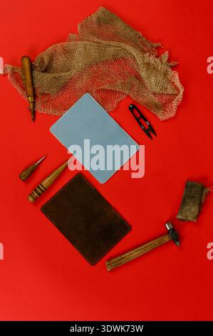 Various leather crafting tools and materials, including two leather pieces and multiple tools, are arranged on a vibrant red background Stock Photo