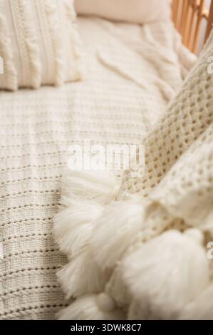 Close up of cream knitted blanket with tassels on cozy bed Stock Photo
