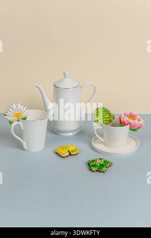 White ceramic teapot and cups arranged with decorative floral cookies on a pastel blue surface, creating a visually appealing tea setting Stock Photo