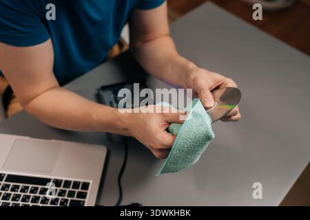 Top view of male hand wiping a cd or dvd with a soft microfiber cloth, maintaining data storage and playback quality for an external disc drive and Stock Photo