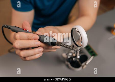 Closeup hand of repairman soldering electronics using a specialized iron and magnifying tool, repairing printed circuit board components, focusing on Stock Photo