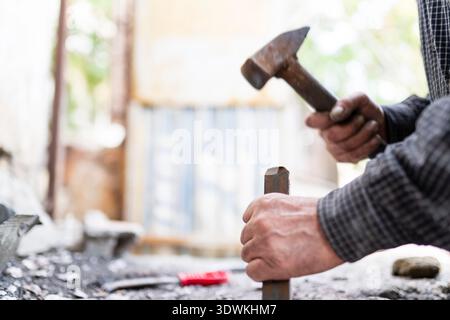 Close-up shot of a man breaking down a wall using a hammer and chisel. Stock Photo