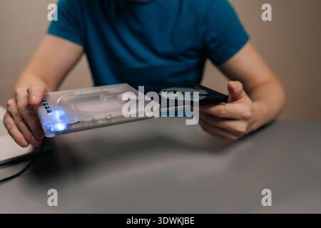 Closeup hand of person holding transparent external optical drive with open disc tray connected to laptop on desk, demonstrating portable dvd cd Stock Photo
