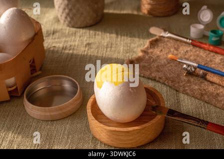 Easter DIY egg decorating process with painting tools white eggs and colorful paints in warm rustic setting Stock Photo