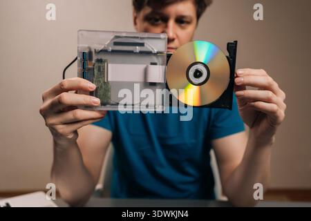 Man holding and presenting external optical disc drive with a transparent casing, revealing its internal components alongside a loaded disc Stock Photo
