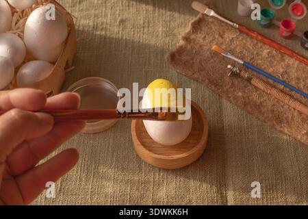 Hand painting Easter egg with yellow paint and brush on rustic fabric background Stock Photo