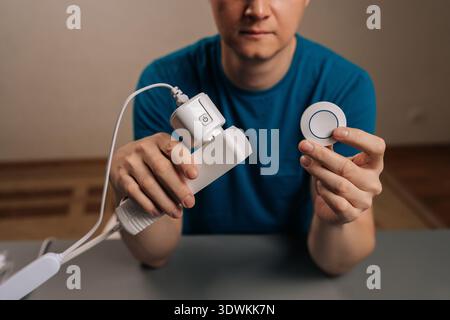 Cropped shot of person holding white smart socket adapter plugged into a power strip and a remote control button for smart automation of modern home Stock Photo