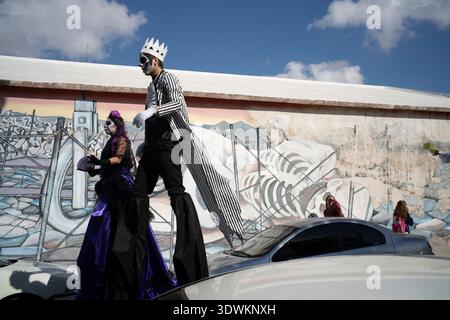 Costumed people on stilts walking street past mural Stock Photo