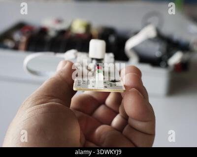 The image shows a small printed circuit board (PCB) held in a hand, containing electronic components. Stock Photo