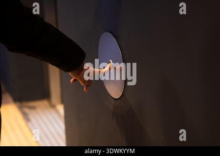 Human hand pressing a sleek, round, metallic button for an elevator or automatic door Stock Photo