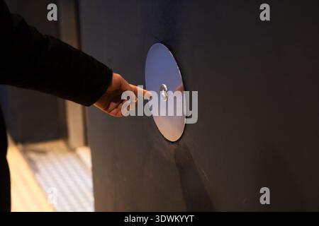 Person's hand reaching and pressing a circular floor selection button inside an elevator Stock Photo