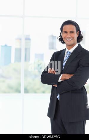Man posing arms-crossed smiling in pinstripe suit with blue tie in office by mullions, copy space. Executive, portrait, corporate, professional, urban Stock Photo