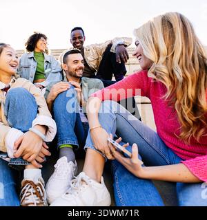 Group of young diverse student friends sitting on campus stairs talking together Stock Photo