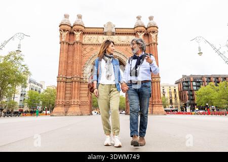 Senior couple traveling barcelona holding hands near historic arch Stock Photo