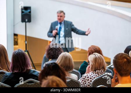 Business speaker presents to attentive audience at conference, corporate seminar atmosphere, leadership and communication focus, networking and professional development. Stock Photo