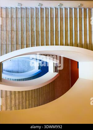 Curved modern staircase interior with marble walls, bold geometric lines, layered arches and rhythmic steps creating abstract architectural pattern and minimalist composition. Stock Photo