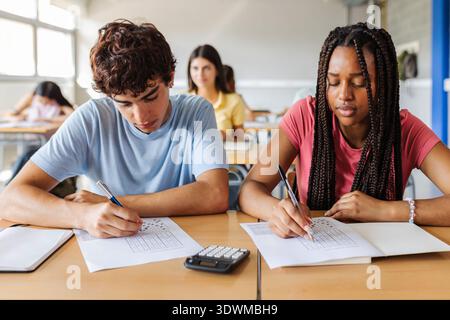 Two students writing exam together at desk Stock Photo