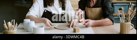 Header of Young and Senior Women Shaping Clay Together Indoors Stock Photo