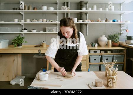 Young Adult Woman Sculpting Clay Slab While Concentrating Indoors Stock Photo