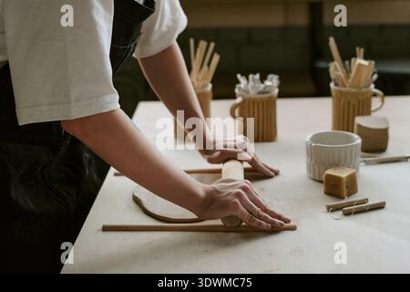 Young Adult Woman Shaping Clay with Rolling Pin during Pottery Workshop Stock Photo