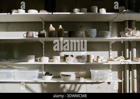 Ceramic Bowls and Vases Arranged on Shelves in Sunlit Pottery Studio Stock Photo