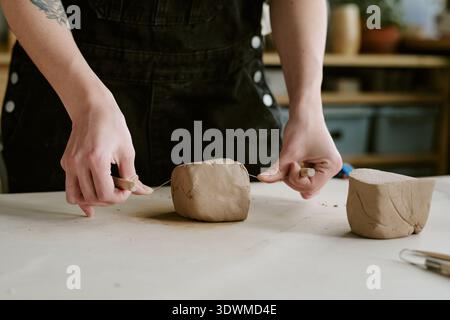 Young Adult Woman Shaping Clay with Wire Cutter in Pottery Studio Stock Photo