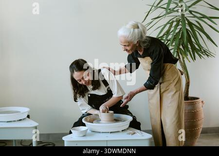 Senior Woman Teaching Young Adult Woman Shaping Clay on Pottery Wheel Stock Photo