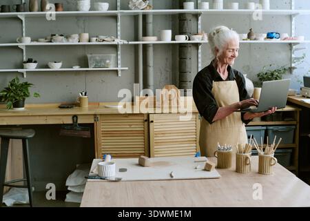 Senior Woman Using Laptop While Working in Ceramics Studio Stock Photo