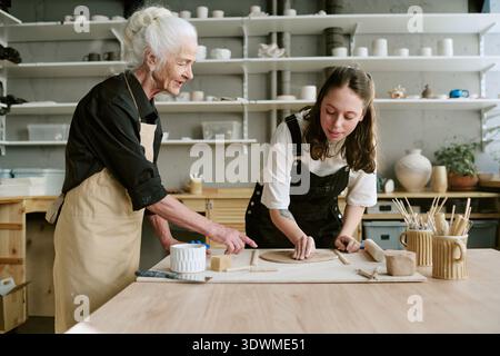 Senior Woman Guiding Young Adult Woman Shaping Clay Stock Photo
