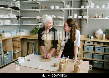 Senior Woman Smiling While Instructing Young Adult Woman in Pottery Stock Photo