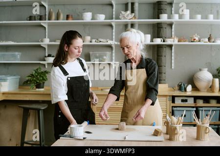 Senior Woman Explaining Pottery Techniques to Young Adult Woman Stock Photo