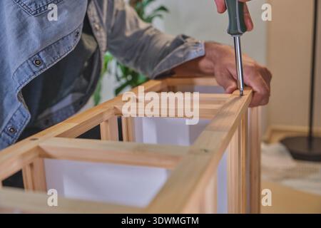 Person is using a screwdriver to assemble a piece of wooden furniture, focusing on diy and home improvement Stock Photo