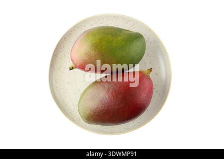 Two whole ripe mango Palmer fruits on retro plate isolated on white background. Stock Photo