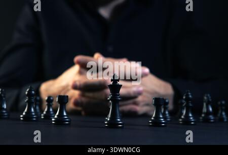Close up of a man playing chess with black chess pieces on the table Stock Photo