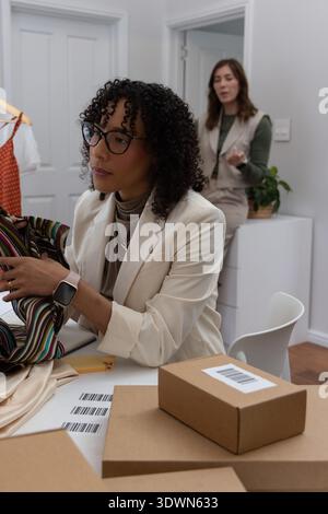 Diverse female team packing orders, applying labels, checking striped garment in studio, copy space Stock Photo