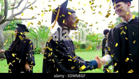 Shaking hands two graduates celebrating on campus lawn, gold confetti, black gowns mortarboard caps Stock Photo