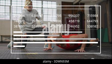 Performing man red tank top doing push-ups on rubber gym floor, trainer gray hoodie squatting, HUD Stock Photo