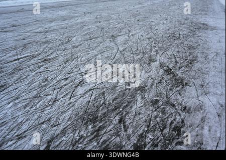A close-up winter photograph of a frozen ice surface covered with numerous skate marks and scratches, lightly dusted with snow, creating abstract line Stock Photo