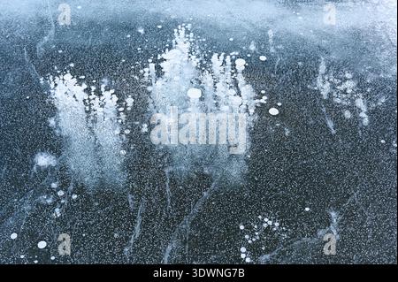 Abstract close-up photograph of frozen lake ice with trapped air bubbles and delicate cracks forming organic patterns beneath a translucent blue-gray Stock Photo