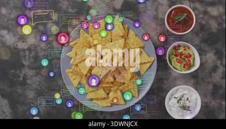 Displaying plate of triangular chips on dark tabletop, 3 bowls salsa, guac, herb dip, chat overlays Stock Photo