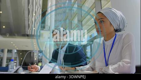 Taking notes woman in headscarf and man in dark suit at conference atrium, with microphones, papers Stock Photo