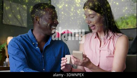Smiling man in blue shirt watching woman in pink blouse opening beige jewelry box, red balloons Stock Photo