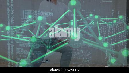 Standing woman wearing white top, gray pants presenting on wall, with green 3D network and code Stock Photo