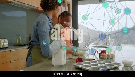 Guiding green-apron mom and orange-top daughter mixing batter in home kitchen with flour and whisk Stock Photo