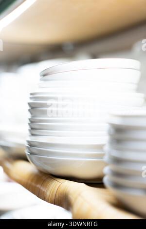 Stacked white ceramic plates on wooden shelf in modern kitchen setting, clean and minimalist design Stock Photo