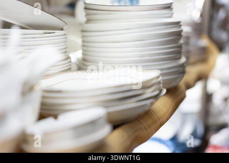 Stacked white ceramic plates on wooden shelf in a kitchenware store, Shanghai China Stock Photo