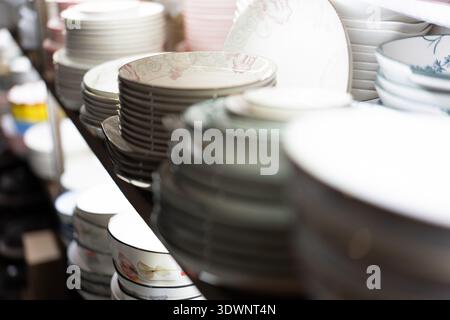Stacks of ceramic plates and bowls displayed on shelves in a shop, blurred background, indoor Stock Photo