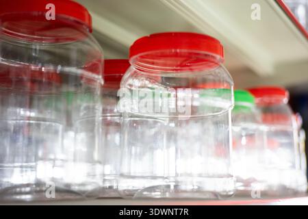Clear plastic jars with red lids lined up on shelf in store, generic retail environment Stock Photo